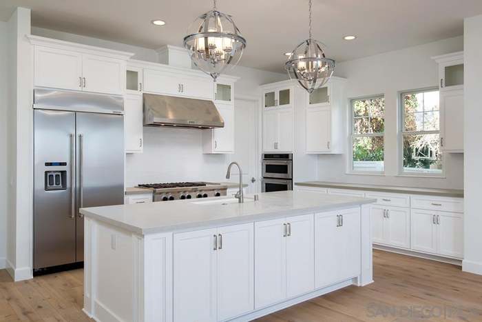 Classic white kitchen remodel with large center island, stainless steel appliances, and elegant chandelier pendant lighting