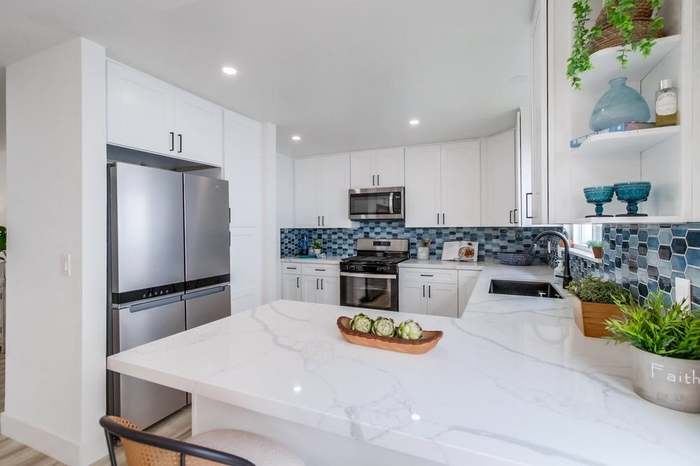 Kitchen remodel with white shaker cabinets, calacatta quartz waterfall island, and blue hexagon tile backsplash